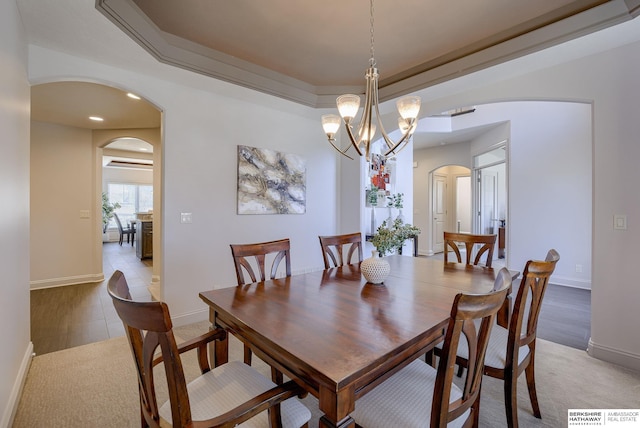 dining room with a raised ceiling, a notable chandelier, recessed lighting, arched walkways, and baseboards