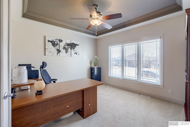 office featuring baseboards, visible vents, a tray ceiling, ceiling fan, and light carpet