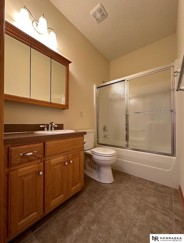 full bathroom featuring bath / shower combo with glass door, tile patterned flooring, vanity, toilet, and a textured ceiling