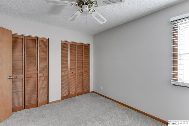 unfurnished bedroom with multiple windows, a textured ceiling, light carpet, and two closets