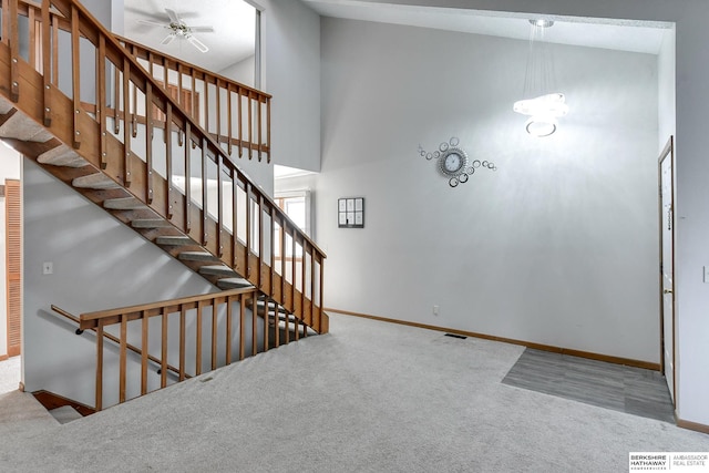 stairs with ceiling fan, carpet flooring, and high vaulted ceiling