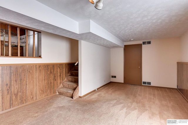 basement with wood walls, a textured ceiling, and light colored carpet