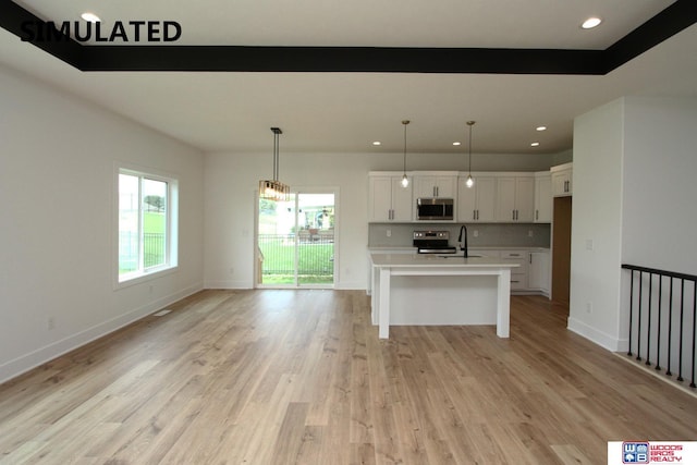 kitchen featuring appliances with stainless steel finishes, a center island with sink, white cabinets, and decorative light fixtures