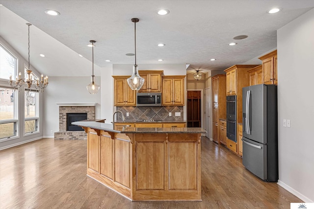 kitchen featuring appliances with stainless steel finishes, a fireplace, a breakfast bar area, decorative backsplash, and hanging light fixtures