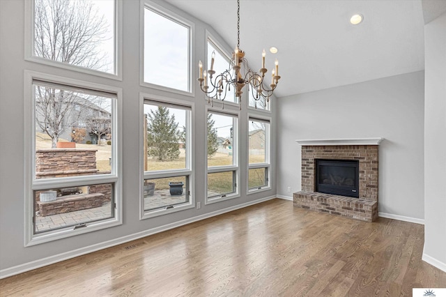 unfurnished living room featuring wood-type flooring, a fireplace, high vaulted ceiling, and a notable chandelier