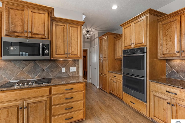 kitchen featuring light hardwood / wood-style flooring, stainless steel appliances, tasteful backsplash, a textured ceiling, and dark stone counters