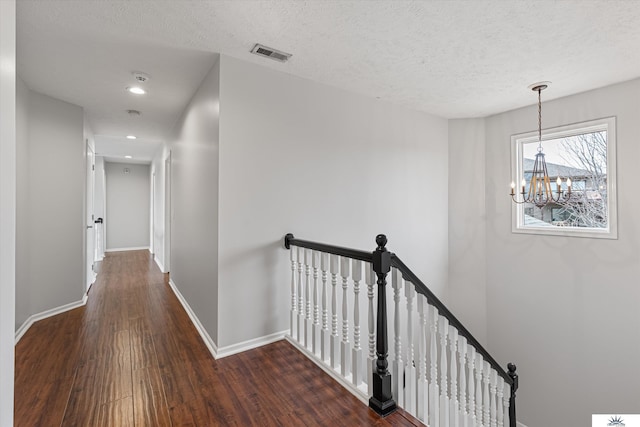 hallway with dark hardwood / wood-style floors, a textured ceiling, and a notable chandelier