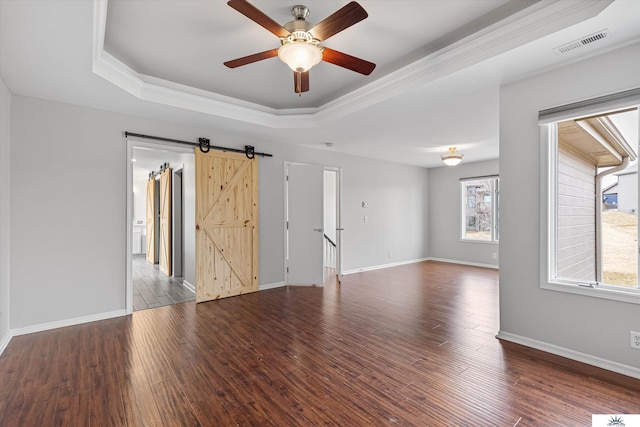 spare room featuring a raised ceiling, wood-type flooring, a barn door, and ornamental molding