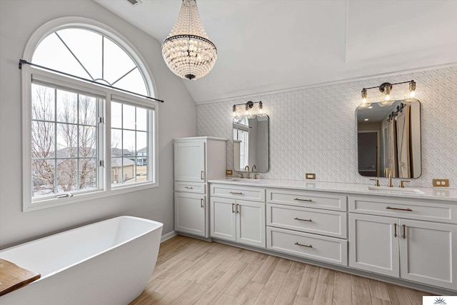 bathroom with a bathing tub, vaulted ceiling, wood-type flooring, and vanity