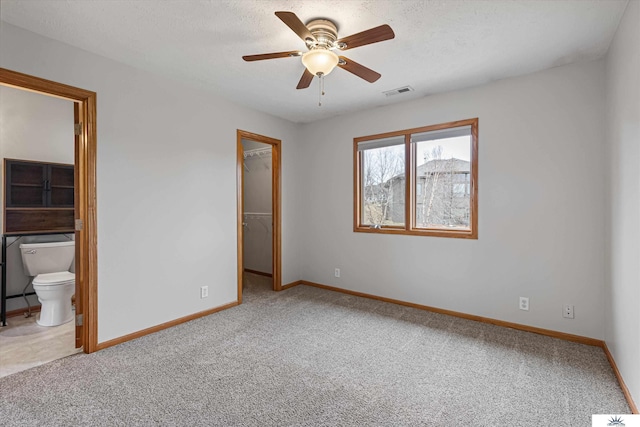 unfurnished bedroom featuring ensuite bathroom, carpet flooring, a textured ceiling, a spacious closet, and a closet