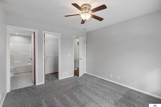 unfurnished bedroom with ensuite bathroom, ceiling fan, dark carpet, a textured ceiling, and a closet