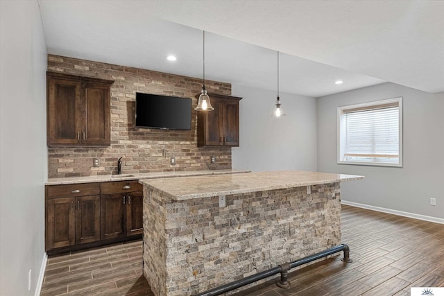 bar with hanging light fixtures, tasteful backsplash, light stone countertops, and dark brown cabinetry