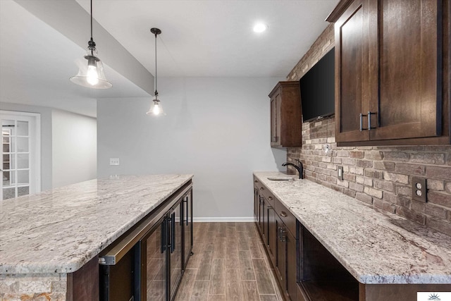 kitchen with tasteful backsplash, light stone countertops, dark brown cabinets, and pendant lighting