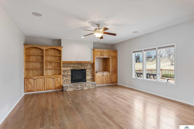 unfurnished living room featuring ceiling fan, a stone fireplace, and light wood-type flooring