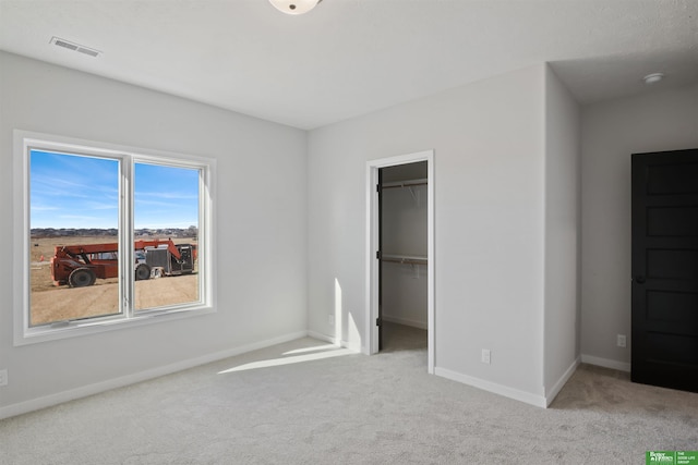 unfurnished bedroom with a walk in closet, light carpet, and a closet