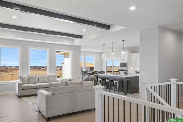 living room with beamed ceiling, sink, and light hardwood / wood-style flooring