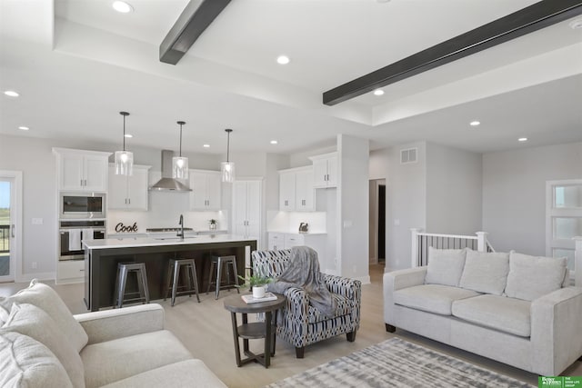 living room featuring beamed ceiling, sink, and light hardwood / wood-style flooring