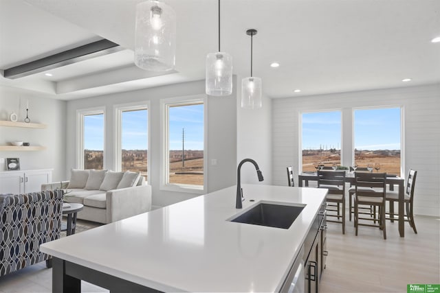 kitchen featuring pendant lighting, sink, a kitchen island with sink, stainless steel dishwasher, and light hardwood / wood-style flooring