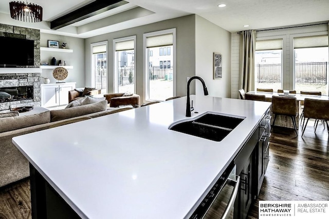 kitchen with a stone fireplace, sink, dark hardwood / wood-style flooring, beam ceiling, and a kitchen island with sink