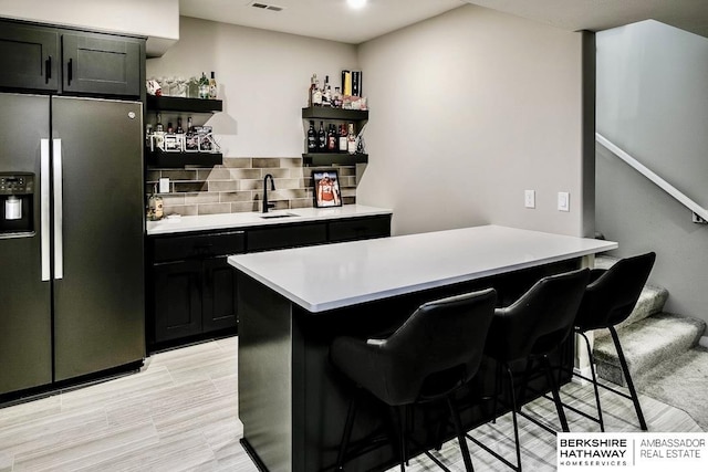 kitchen with a kitchen bar, sink, stainless steel fridge, a kitchen island, and backsplash