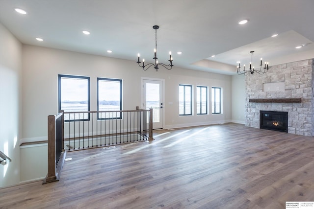 unfurnished living room featuring a wealth of natural light, a stone fireplace, hardwood / wood-style floors, and a chandelier