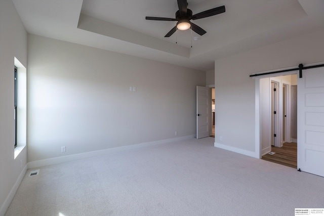 unfurnished bedroom featuring ceiling fan, a tray ceiling, a barn door, and carpet floors