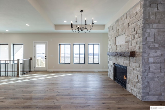 unfurnished living room featuring hardwood / wood-style flooring, a stone fireplace, a raised ceiling, and a chandelier