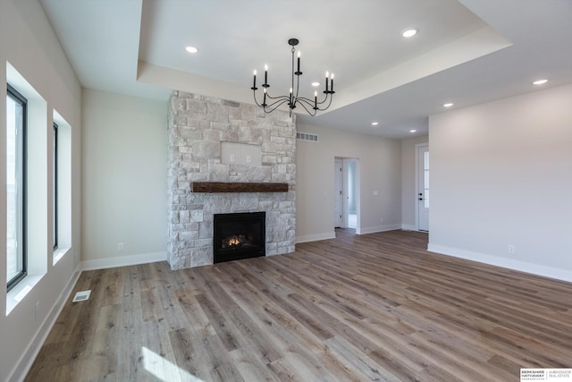 unfurnished living room featuring a tray ceiling, a stone fireplace, light hardwood / wood-style flooring, and a notable chandelier