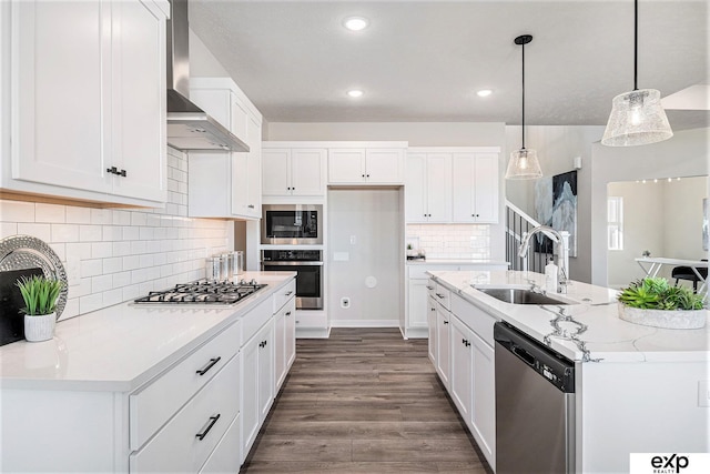 kitchen featuring wall chimney range hood, sink, appliances with stainless steel finishes, white cabinets, and decorative light fixtures