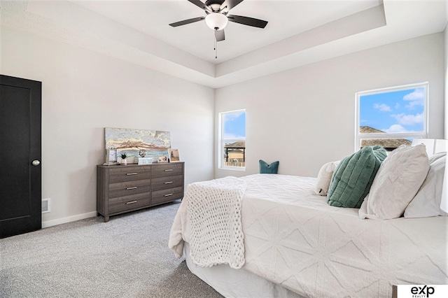 carpeted bedroom featuring ceiling fan, a tray ceiling, and multiple windows