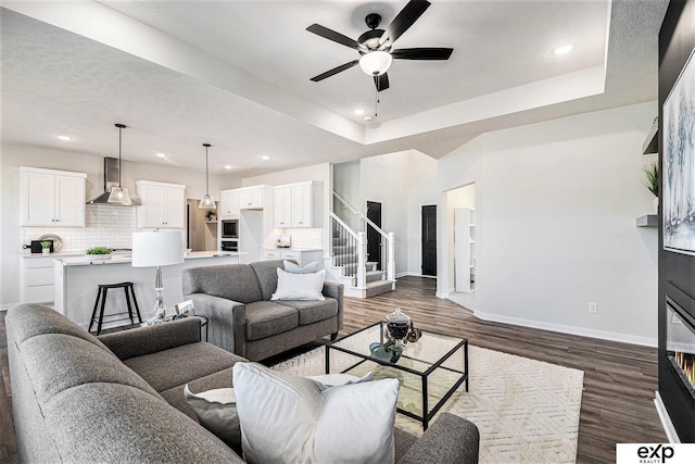 living room with ceiling fan, a tray ceiling, and dark hardwood / wood-style flooring