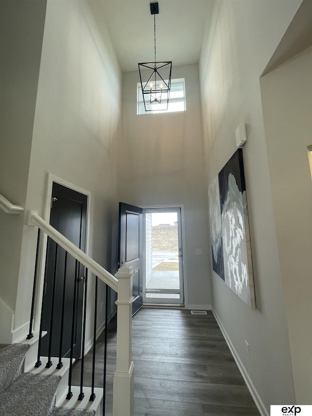 entryway featuring a notable chandelier, a towering ceiling, and dark wood-type flooring