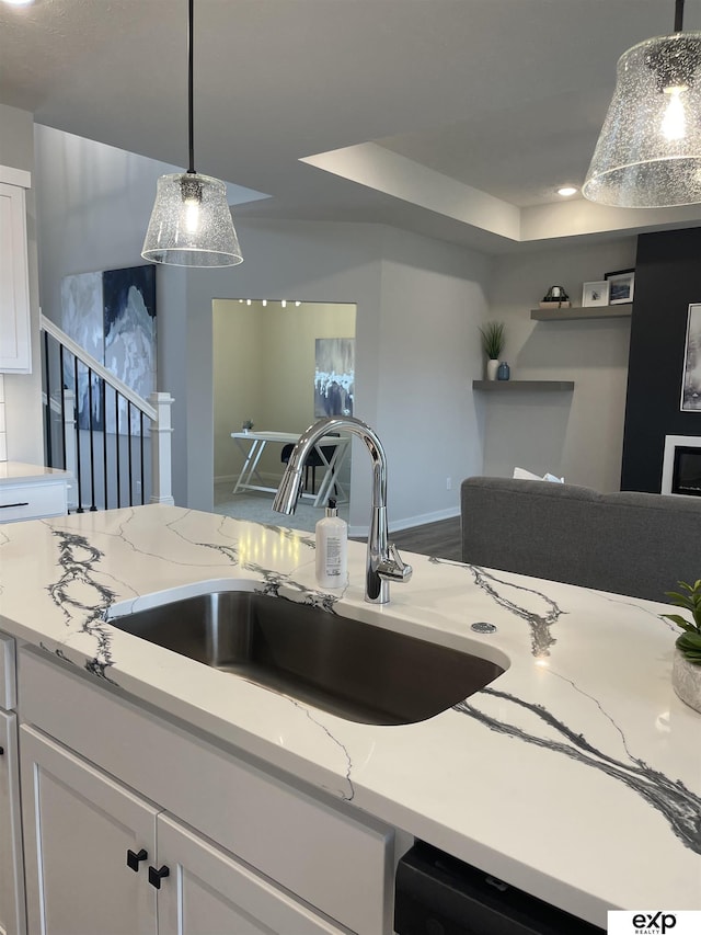 kitchen featuring pendant lighting, light stone countertops, sink, and white cabinets