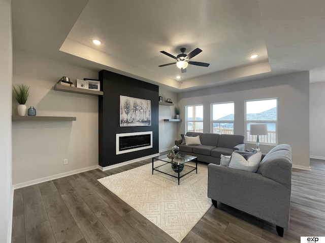 living room with a tray ceiling, dark wood-type flooring, and ceiling fan