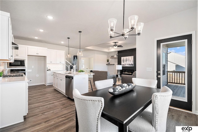 dining space with sink, ceiling fan with notable chandelier, a large fireplace, and dark hardwood / wood-style floors