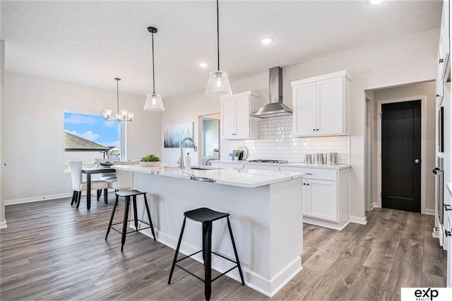 kitchen with wall chimney exhaust hood, sink, white cabinets, a kitchen island with sink, and backsplash