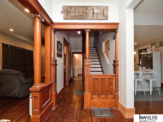 hall with dark hardwood / wood-style flooring, a textured ceiling, and ornate columns