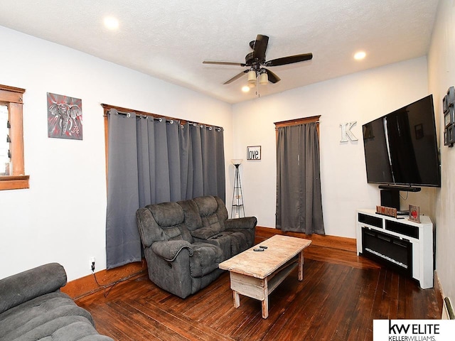 living room featuring dark wood-type flooring, a textured ceiling, and ceiling fan