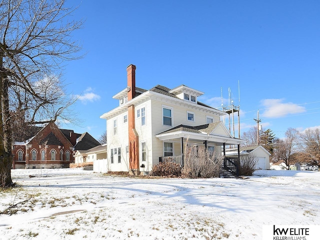 snow covered rear of property with an outbuilding, a garage, and a porch