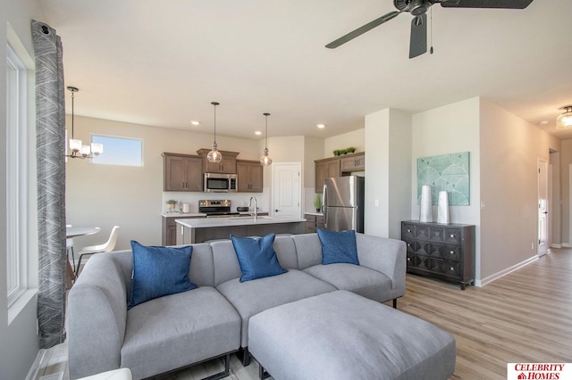 living room featuring ceiling fan with notable chandelier, sink, and light wood-type flooring