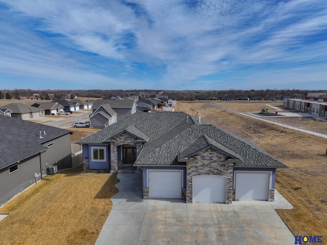 view of front of home with a garage, central AC, driveway, stone siding, and a residential view