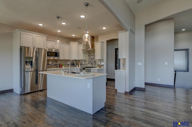 kitchen featuring wall chimney exhaust hood, dark wood-type flooring, a kitchen island with sink, stainless steel appliances, and light countertops