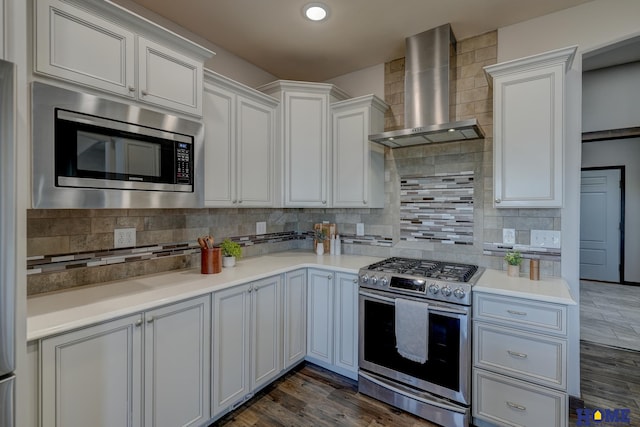 kitchen featuring stainless steel appliances, wall chimney range hood, dark wood finished floors, and decorative backsplash