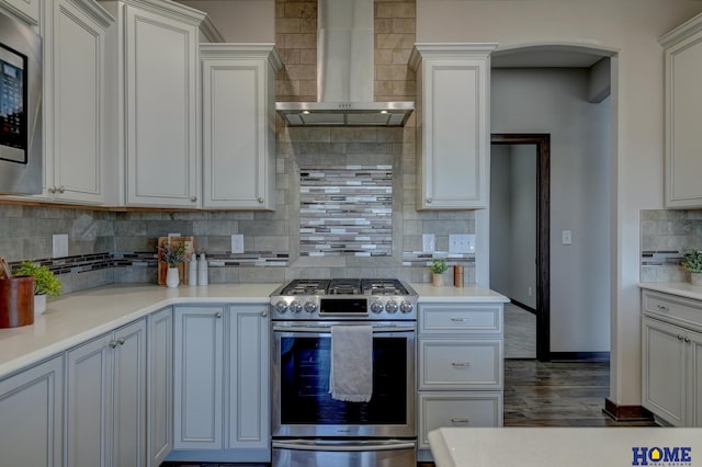 kitchen with baseboards, decorative backsplash, appliances with stainless steel finishes, light countertops, and wall chimney range hood