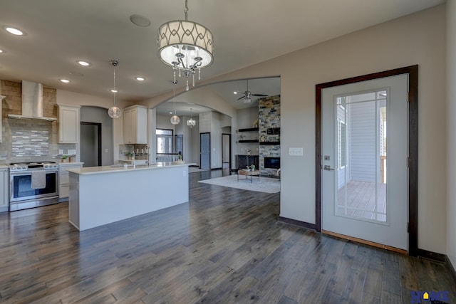 kitchen featuring white cabinets, dark wood-style flooring, light countertops, wall chimney range hood, and stainless steel range with gas cooktop