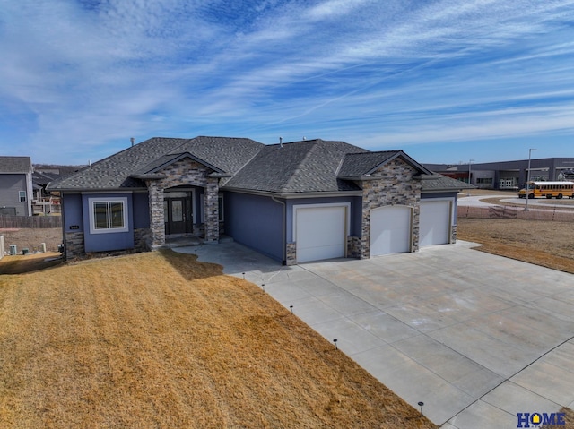 view of front of house featuring roof with shingles, concrete driveway, an attached garage, a front yard, and stone siding