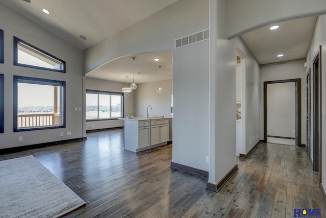 kitchen with arched walkways, dark wood-style flooring, light countertops, visible vents, and a sink