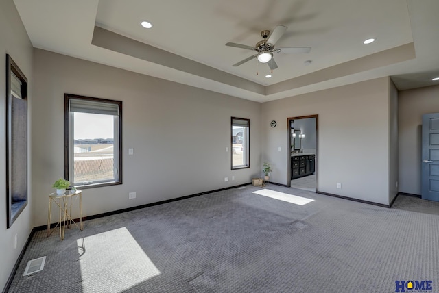 carpeted spare room with a wealth of natural light, a tray ceiling, visible vents, and baseboards