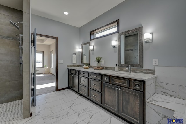 bathroom featuring marble finish floor, double vanity, a sink, tiled shower, and baseboards