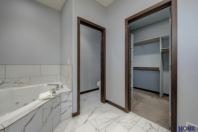 bathroom featuring a walk in closet, marble finish floor, toilet, a whirlpool tub, and baseboards